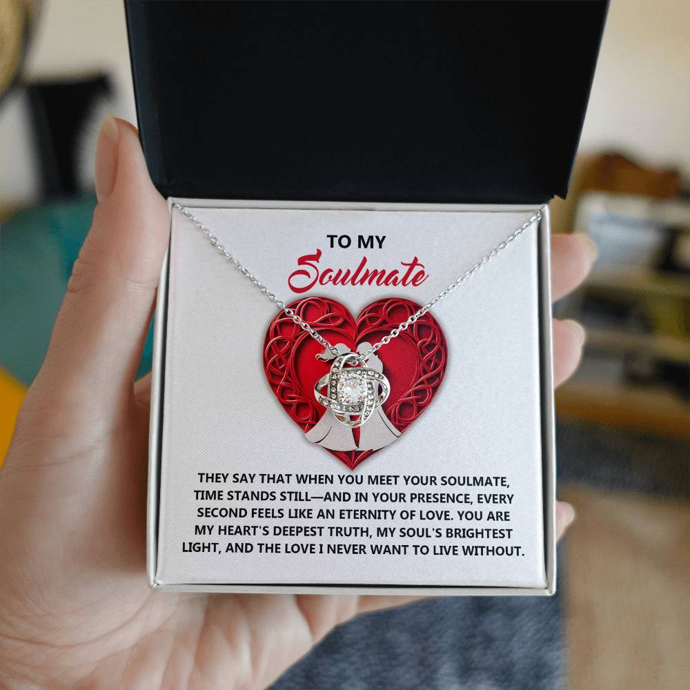 A hand presents a necklace box with the Soulmate-Deepest Truth Love Knot Necklace, featuring a heart pendant and sparkling cubic zirconia. The box reads "To My Soulmate" and contains a heartfelt message about love and connection—an ideal personalized gift.