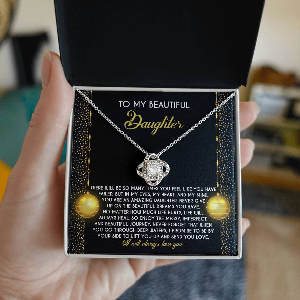 A hand holds an open jewelry box showcasing the exquisite Daughter-Deep Waters Love Knot Necklace, embellished with cubic zirconia crystals and featuring a heartfelt message for a daughter.