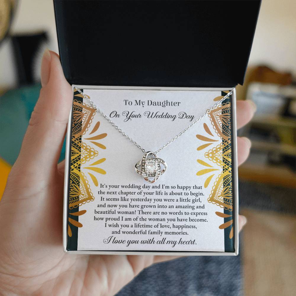 The "To Daughter, Wedding - A Little Girl - Love Knot Necklace" adorned with cubic zirconia crystals is elegantly showcased in a box containing a heartfelt message for a daughter on her wedding day. The text conveys love, pride, and best wishes for a joyful marriage, beautifully accentuated by the option of a white gold or yellow gold finish.