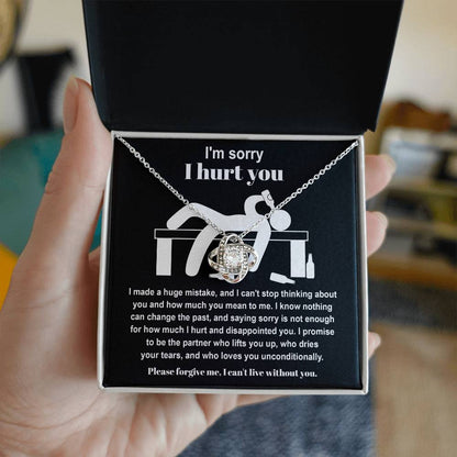 The Sorry-Change The Past 2 - Love Knot Necklace, featuring a pendant adorned with cubic zirconia crystals, is gracefully showcased on black fabric. It includes an apology message addressing past hurt and a heartfelt plea for forgiveness, complemented by illustrations of a distressed figure.