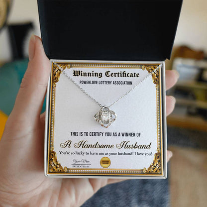 A "To Wife, Winning Certificate - Love Knot Necklace" is displayed against a certificate text background reading, "Winning Certificate - Powerlove Lottery Association - A Handsome Husband," featuring shimmering cubic zirconia crystals and an elegant gold finish.