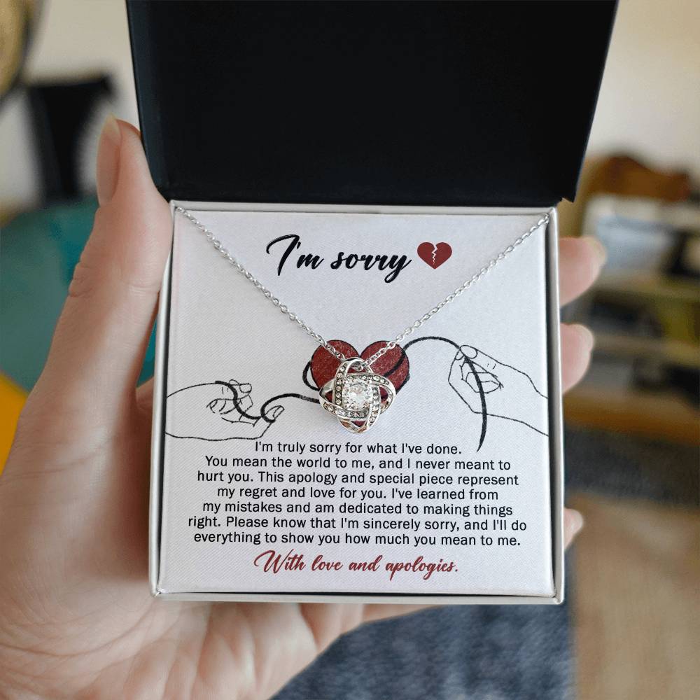 The Sorry-Mean The World - Love Knot Necklace, crafted from white gold and adorned with a heart-shaped pendant, is displayed on a card. This card conveys an apology message expressing regret and dedication to making things right, ending with "With love and apologies." The necklace is embellished with sparkling cubic zirconia crystals that add a touch of elegance.