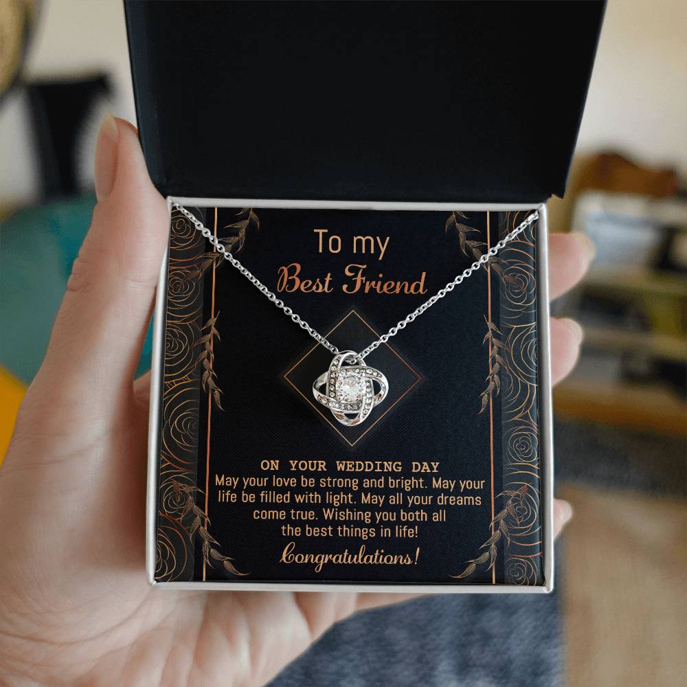 A "To Best Friend Wedding, Strong And Bright - Love Knot Necklace" adorned with cubic zirconia crystals is elegantly displayed on a black card that reads, "To my Best Friend on your wedding day. Congratulations!" The card features a decorative gold border and highlights the necklace's white gold or yellow gold finish options.