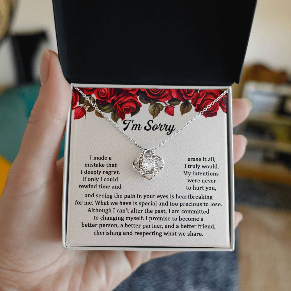 The "Sorry, Precious To Lose - Love Knot Necklace," adorned with cubic zirconia crystals, is displayed on a card featuring an apology message set against a background of red roses. The message expresses regret and a commitment to change.