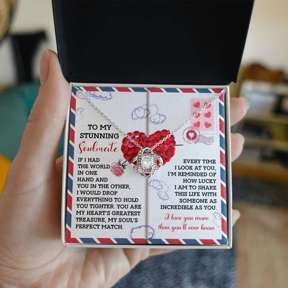 A hand holds an open box with a "Soulmate-Perfect Match - Love Knot Necklace," adorned with cubic zirconia crystals and accompanied by a card bearing a printed love message.