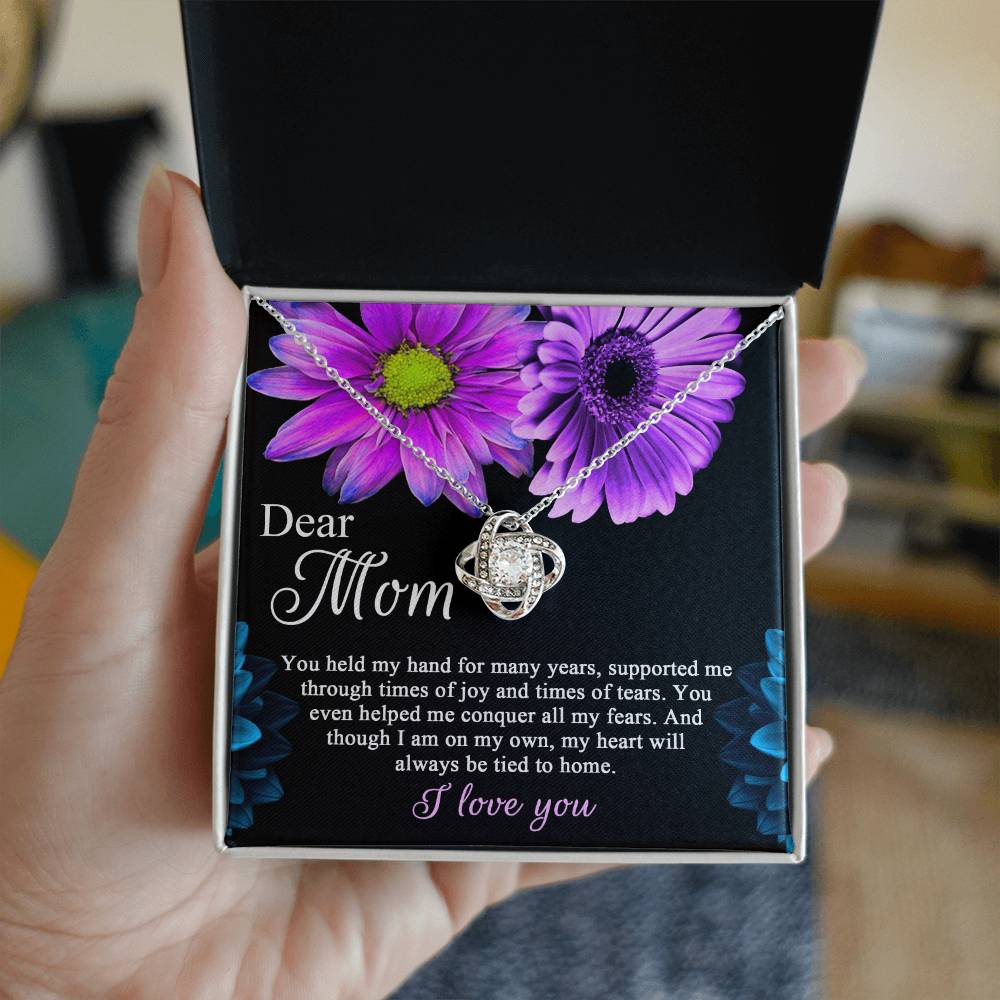 Open the gift box containing the "To Mom, Held My Hand - Love Knot Necklace," featuring a spherical pendant adorned with cubic zirconia crystals. The necklace is presented on a card decorated with purple flowers and bears the message: "Dear Mom, You held my hand for many years, supported me... I love you.