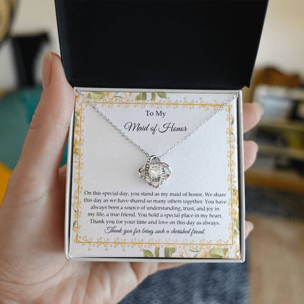 Presenting the "To Maid of Honor, Share This Day - Love Knot Necklace," featuring a stunning pendant adorned with cubic zirconia crystals and finished in white gold. It is beautifully displayed in a box embellished with a floral border and includes a heartfelt message expressing gratitude and appreciation to the "Maid of Honor.