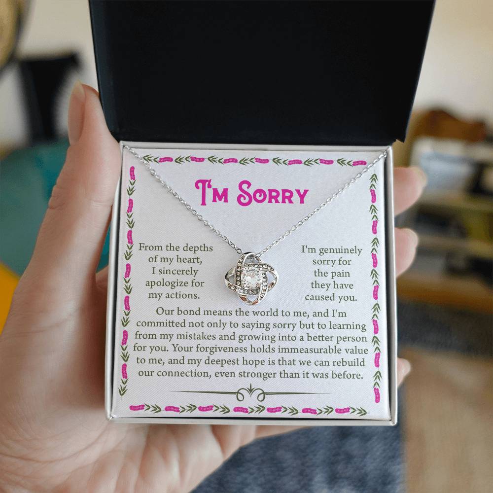 A person holds an open jewelry box containing a "Sorry-A Better Person - Love Knot Necklace" adorned with shimmering cubic zirconia crystals and accompanied by a heartfelt message, expressing sincere regret for their actions and a commitment to personal growth and reconciliation.