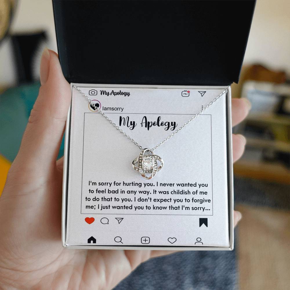 The "Sorry-My Apology - Love Knot Necklace," featuring a white gold finish and sparkling cubic zirconia crystals, is elegantly displayed in a box. The background includes an emotional apology message presented as a simulated social media post.