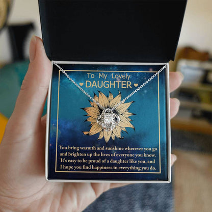 The "To Daughter, Be Proud Of - Love Knot Necklace" showcases a stunning pendant with intertwined rings adorned with cubic zirconia crystals, elegantly presented against a background featuring a sunflower and a heartfelt message to a daughter.