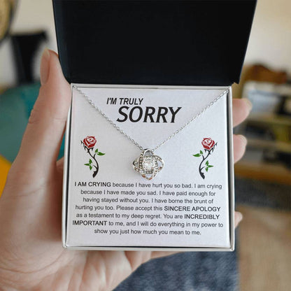 The Sorry-Made You Sad - Love Knot Necklace, crafted in silver with an interlocking design, is presented on a card featuring an apology message and accompanied by two red roses. The text conveys profound regret and vows to make things right, while the cubic zirconia crystals enhance the elegance of this heartfelt gesture.