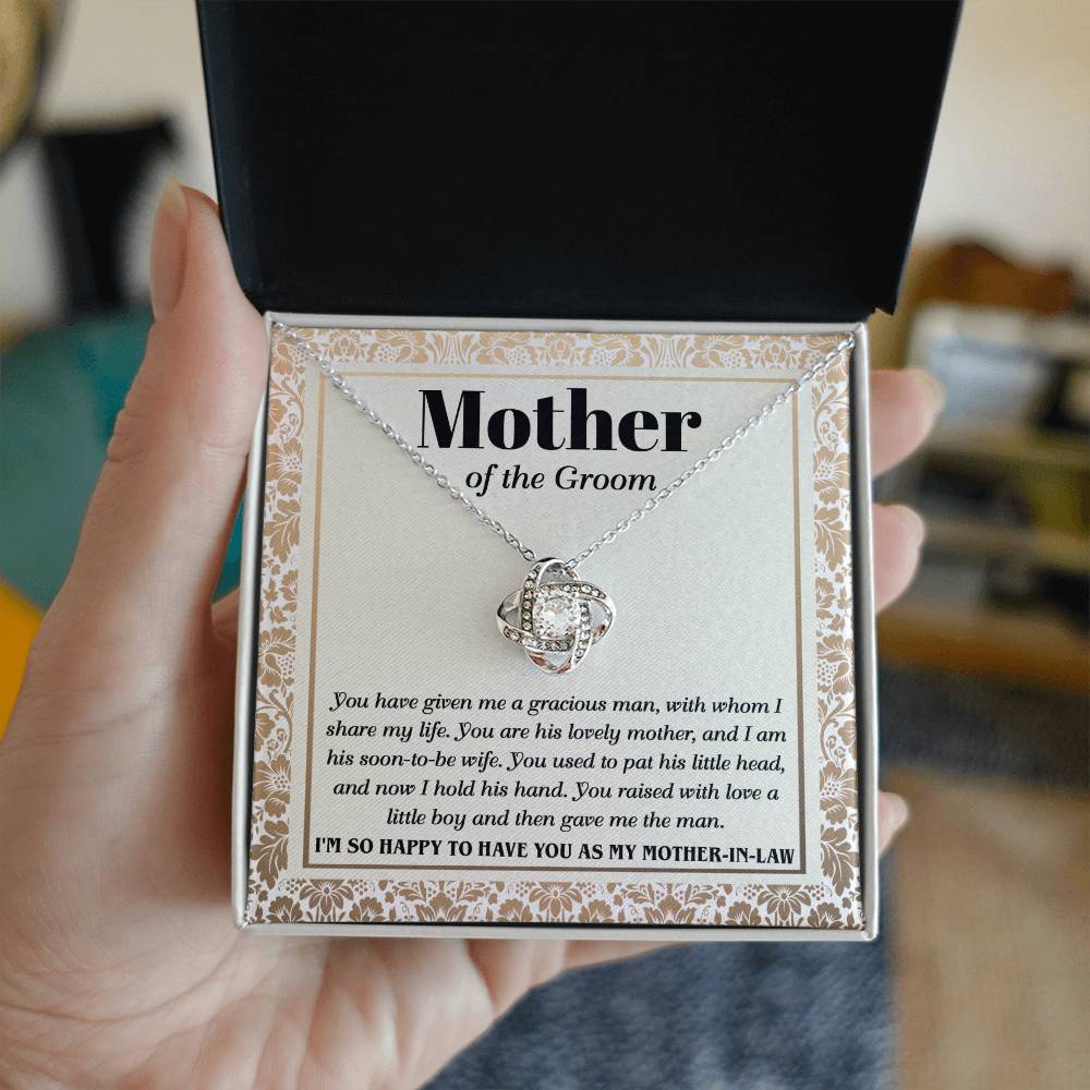 A "To Mother-In-Law, To Have You - Love Knot Necklace" with a heart-shaped pendant adorned with cubic zirconia crystals on a card labeled "Mother of the Groom" with a loving message expressing gratitude from the groom.