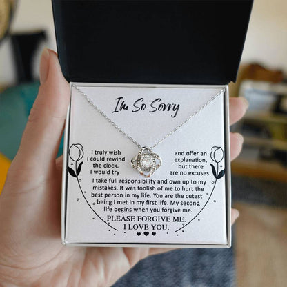 A person holds an open jewelry box containing a stunning Sorry-My First Life - Love Knot Necklace adorned with cubic zirconia crystals and a printed apology note with an "I'm So Sorry" message.