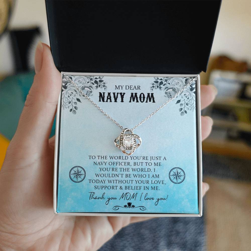 A hand is holding a gift box with an 18k yellow gold My Dear Navy Mom, To The World You're Just A Navy Officer - Love Knot Necklace and a message inside the lid dedicated to a "navy mom," expressing personal gratitude and love from ShineOn Fulfillment.