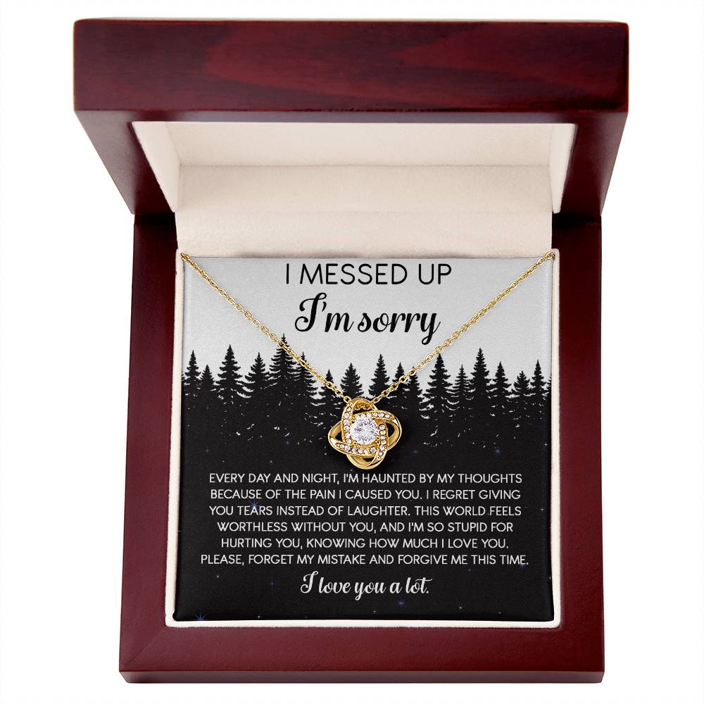 The Sorry-By My Thoughts - Love Knot Necklace, featuring a heart-shaped pendant adorned with cubic zirconia crystals, is displayed on a card with an apology message. The card reads: "I messed up. I'm sorry. Every day and night, I'm haunted...I love you a lot," set against a serene forest background.