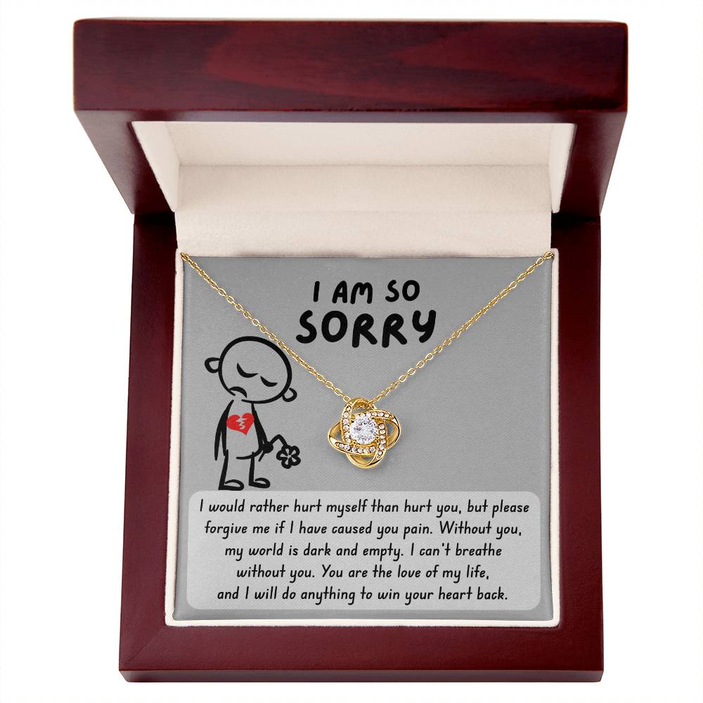 The Sorry-Dark And Empty - Love Knot Necklace, made of 14k white gold and adorned with cubic zirconia crystals, is displayed in a wooden box. The box has a message that reads, "I am so sorry," with a heartfelt apology note printed underneath.