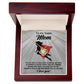 The "Mom-A Fearless Woman" Love Knot Necklace in gold finish features a circular pendant with a clear cubic zirconia, presented in a wooden box. The inner lid card displays a silhouette of a woman in a red cape and the message "to Super Mom.