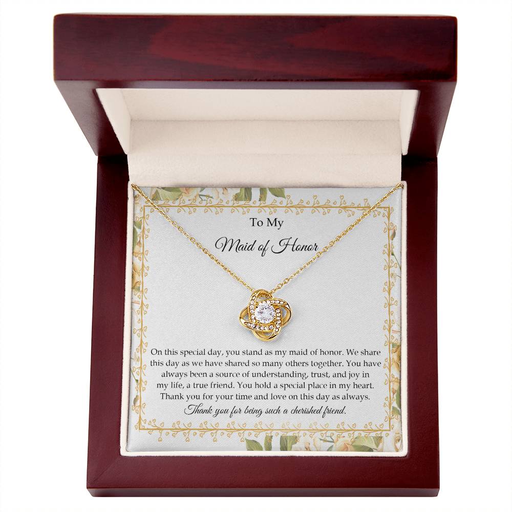 Presenting the "To Maid of Honor, Share This Day - Love Knot Necklace," featuring a stunning pendant adorned with cubic zirconia crystals and finished in white gold. It is beautifully displayed in a box embellished with a floral border and includes a heartfelt message expressing gratitude and appreciation to the "Maid of Honor.