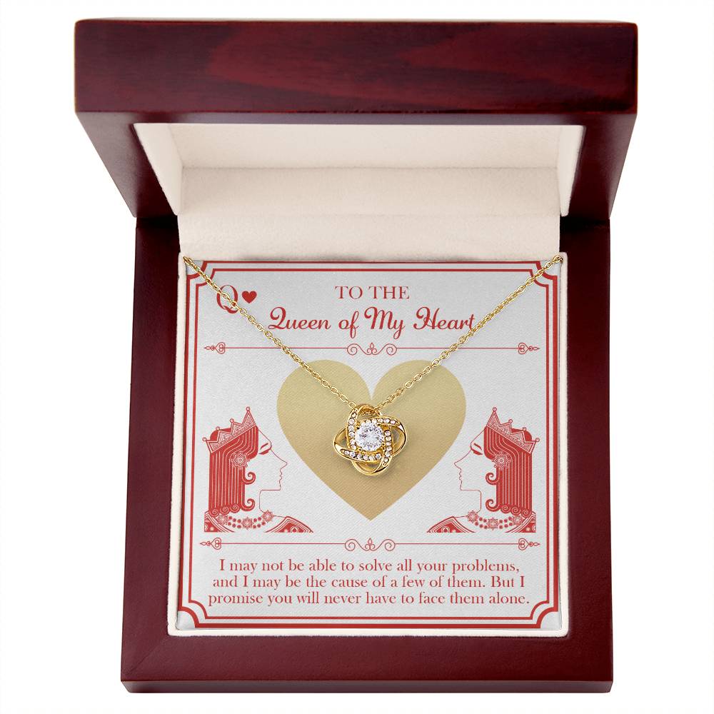 A "To Wife, The Queen - Love Knot Necklace" with a central gemstone is elegantly showcased in an open wooden jewelry box. The interior includes a card adorned with an illustration of a heart and two queens, along with a heartfelt message that reads "To the Queen of My Heart" and a loving note below, all enhanced by cubic zirconia crystals.