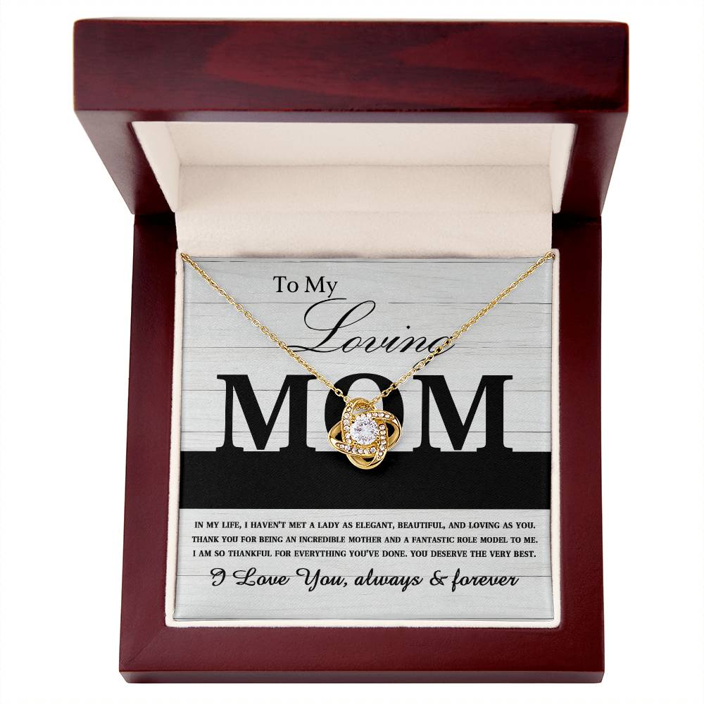 The "To Mom, Loving As You - Love Knot Necklace" adorned with cubic zirconia crystals is beautifully displayed inside an open wooden box. The lid of the box features a heartfelt message beginning with "To My Loving MOM" and ending with "I Love You, always & forever." This personalized gift elegantly captures eternal love.