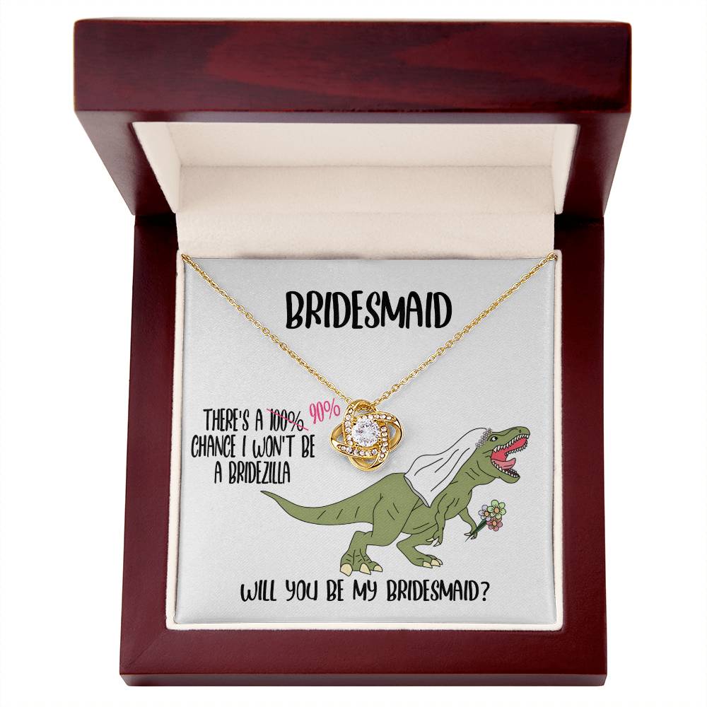 A bridesmaid proposal necklace box featuring a dinosaur with a veil and a stunning To Bridesmaid, Will You Be - Love Knot Necklace in white gold. The text reads, "There's a 90% chance I won't be a bridezilla. Will you be my bridesmaid?