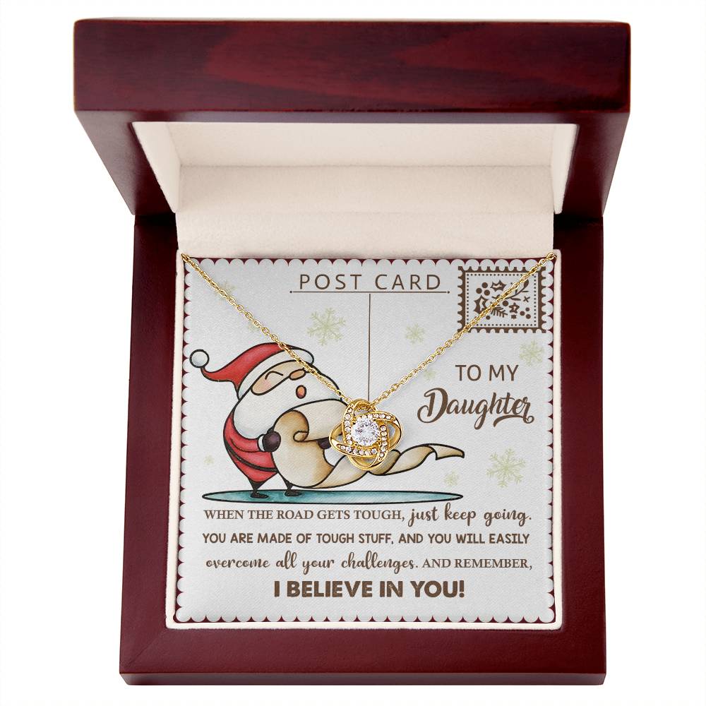 The Daughter-Keep Going - Love Knot Necklace rests in a box, paired with a Santa-themed card addressed to "My Daughter." The heartfelt message highlights the themes of resilience and belief, celebrating the unwavering bond between you both. Embellished with shimmering cubic zirconia, it’s a heartfelt gift.