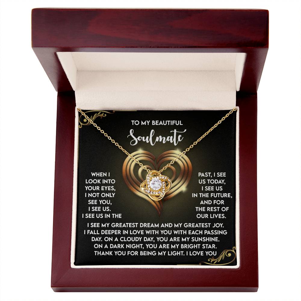 The Soulmate-I See Us Love Knot Necklace with a gold-finished heart pendant is elegantly displayed in a jewelry box. Lifting the lid reveals a romantic message to a soulmate, beautifully layered over a heart design.