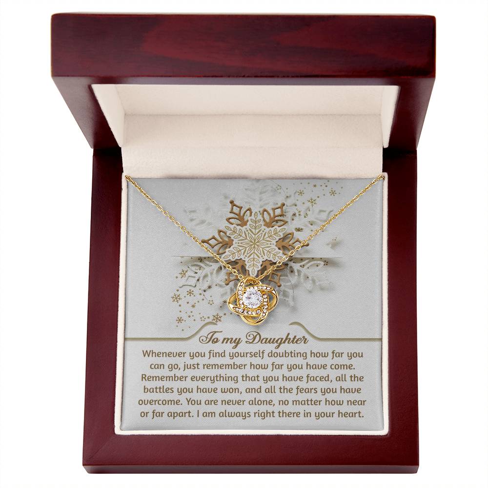 The "Daughter-You Can Go - Love Knot Necklace," featuring a central gemstone to symbolize an unbreakable bond, is elegantly presented in an open wooden box accompanied by a touching message for a daughter.