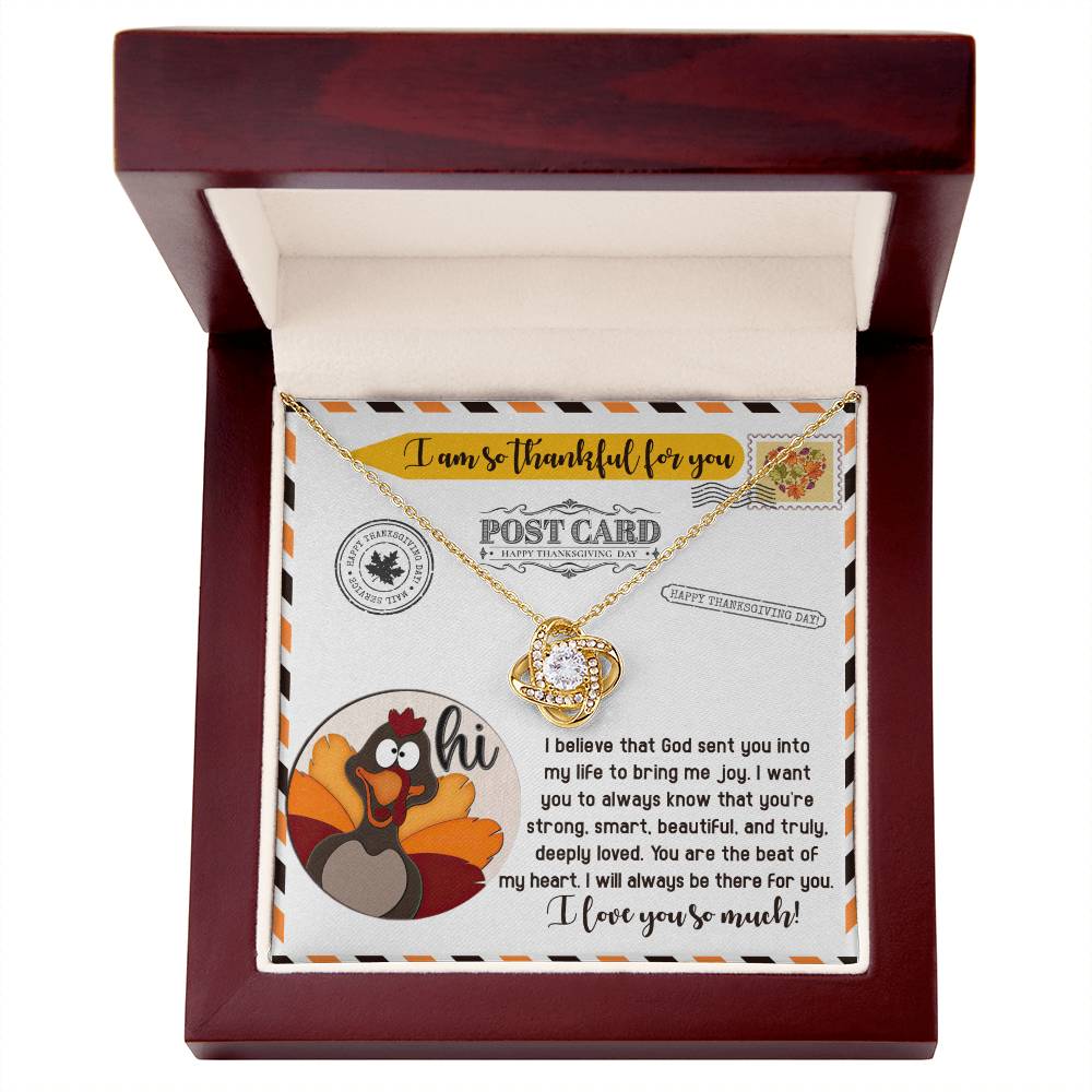 The Thanksgiving-The Beat - Love Knot Necklace, featuring a circular pendant adorned with cubic zirconia, is presented in a box. The box showcases a postcard design that includes a message of gratitude and affection and is decorated with a cartoon turkey.