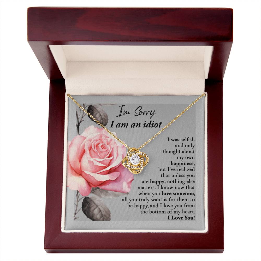 The "Sorry-Love Someone - Love Knot Necklace" is an elegant silver piece with a heart-shaped pendant, adorned with sparkling cubic zirconia crystals. It rests on a beautifully designed box featuring a pink rose and a heartfelt apology note, making it truly a classic gift.