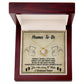 The "Mama To Be-Enjoy The Ride" Love Knot Necklace, adorned with cubic zirconia crystals, comes in a wooden box. Inside the lid are the words "Mama-To-Be," angel illustrations, tiny footprints, and a heartfelt message about parenthood—an ideal personalized gift for expecting mothers.