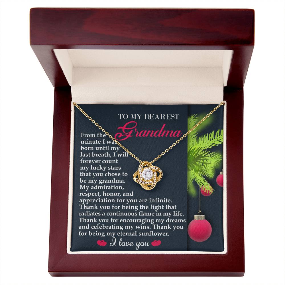 A Grandma-Eternal Sunflower Love Knot Necklace in a gift box, featuring a touching message for a grandmother, beautifully adorned with Christmas ornaments and showcasing a dazzling cubic zirconia set in a white gold finish.