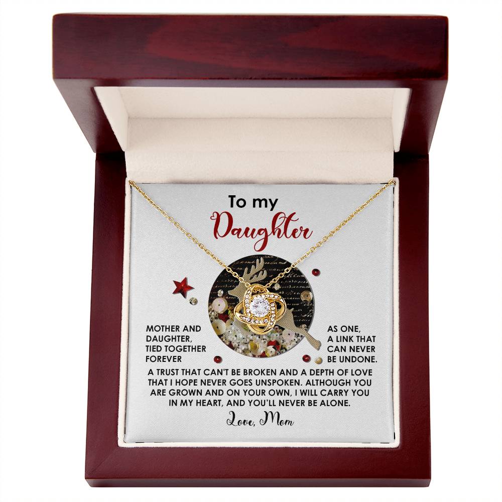 The Daughter-Forever As One - Love Knot Necklace, embellished with cubic zirconia crystals, is gracefully arranged inside an open red box. The lid features a heartfelt message, creating a one-of-a-kind gift.