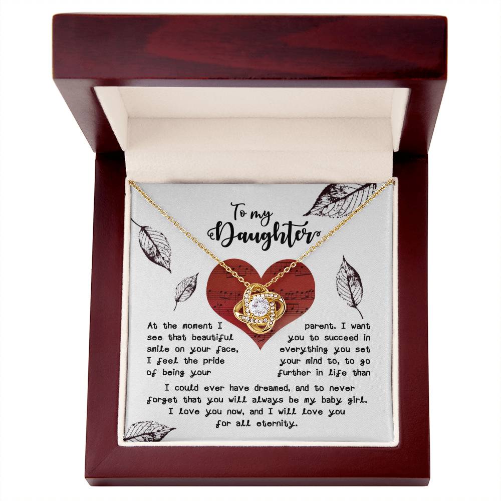 The Daughter-On Your Face - Love Knot Necklace, featuring a heart-shaped pendant adorned with shimmering cubic zirconia crystals, is elegantly displayed in an open box. Inside the box, a heartfelt letter to a daughter adds a touch of sentiment to this exquisite gift.