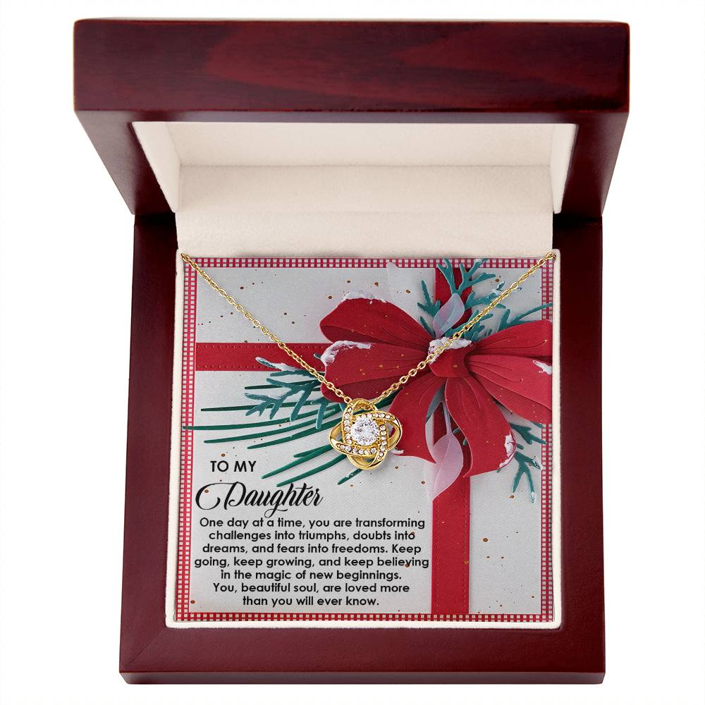 The Daughter-Beautiful Soul - Love Knot Necklace, featuring a circular pendant that glistens with a gold finish, is elegantly nestled inside an open wooden box. The lid of the box includes a message card with a red bow design, creating a sophisticated and heartfelt gift choice.