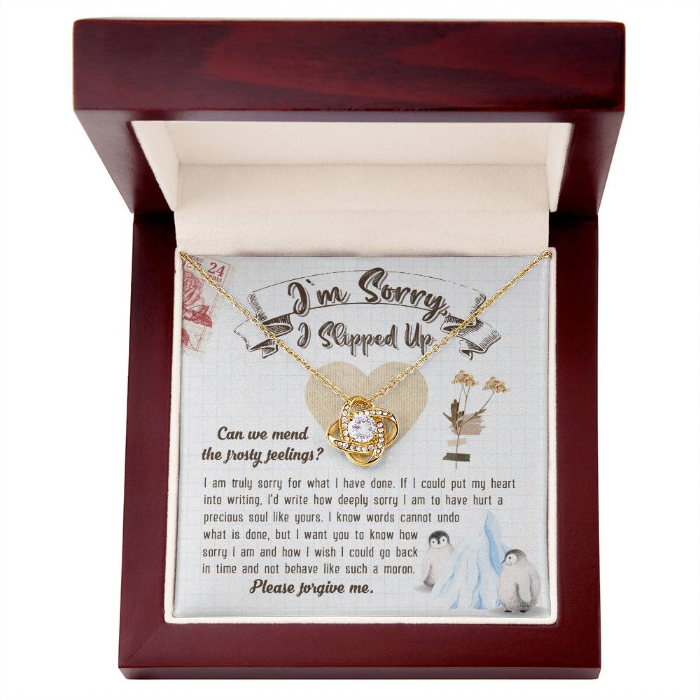 The Sorry-Precious Soul - Love Knot Necklace, featuring an intertwined heart pendant adorned with cubic zirconia crystals, is beautifully displayed in a box. The box comes with an apology note and charming illustrations of flowers, mail stamps, and penguins on a grid-patterned background.