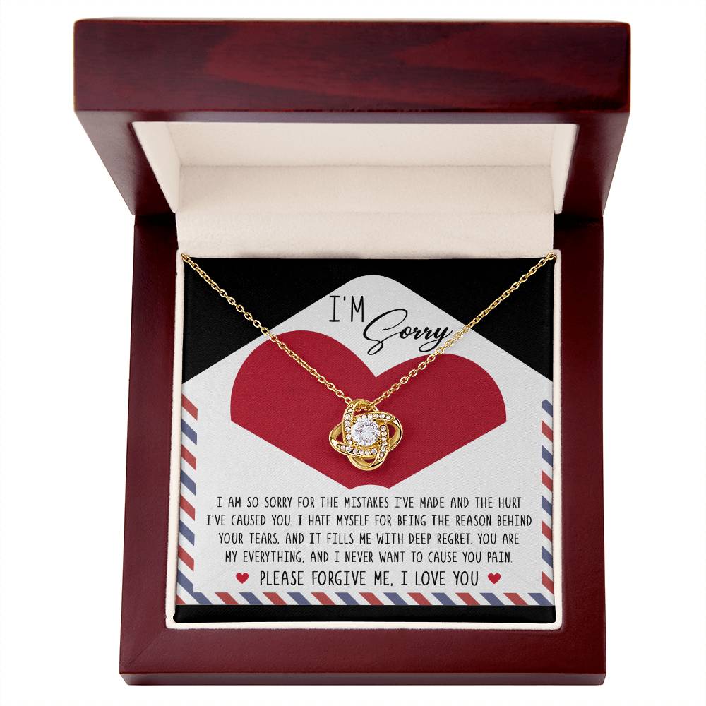 An open jewelry box featuring the "Sorry-Behind Your Tears - Love Knot Necklace," crafted from 14k white gold and embellished with cubic zirconia crystals, is displayed over a card that reads "I'm Sorry" and conveys messages of regret, love, and a heartfelt plea for forgiveness.