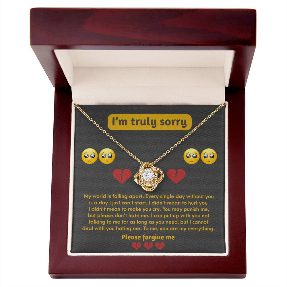 The "Sorry-Make You Cry - Love Knot Necklace" featuring a gemstone pendant is elegantly displayed in an open wooden box. The lid bears an apology message adorned with crying emoji faces, while the 14k white gold and sparkling cubic zirconia crystals add a touch of heartfelt sentiment to this beautiful piece.