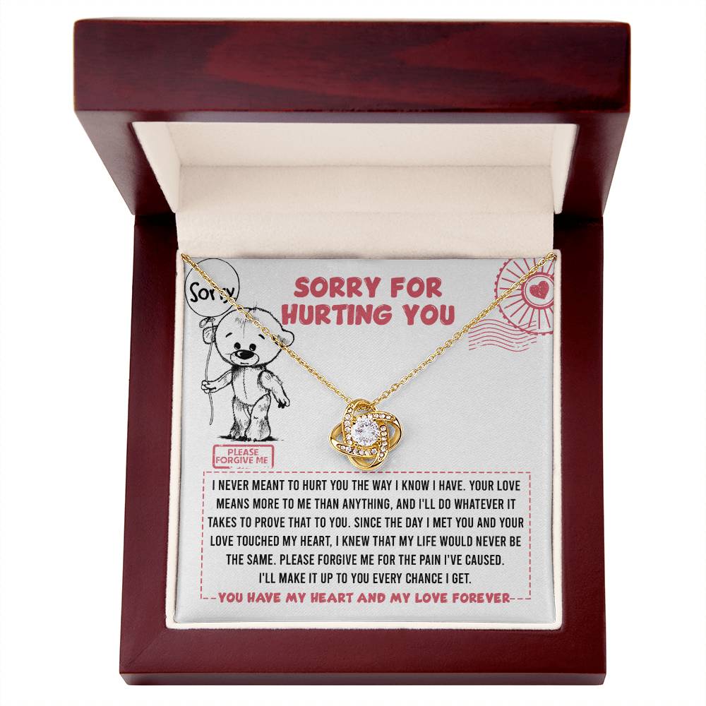 The Sorry-Every Chance - Love Knot Necklace, featuring a gold finish and adorned with cubic zirconia crystals, is elegantly nestled in a wooden box. Inside the box lid is a heartfelt message: "Sorry for hurting you," accompanied by an illustration of a teddy bear holding a heart. An accompanying apology note completes this touching gesture.