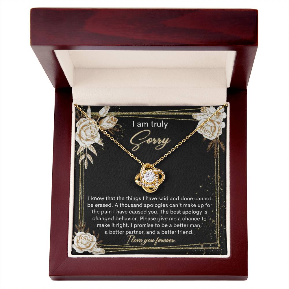 The Sorry-Cannot Be Erased - Love Knot Necklace, adorned with shimmering cubic zirconia crystals and available in a choice of white gold or yellow gold finish, is displayed against a backdrop of a black card bearing an apology message that reads, "I am truly sorry" and "I promise to be a better man, a better partner, and a better friend.