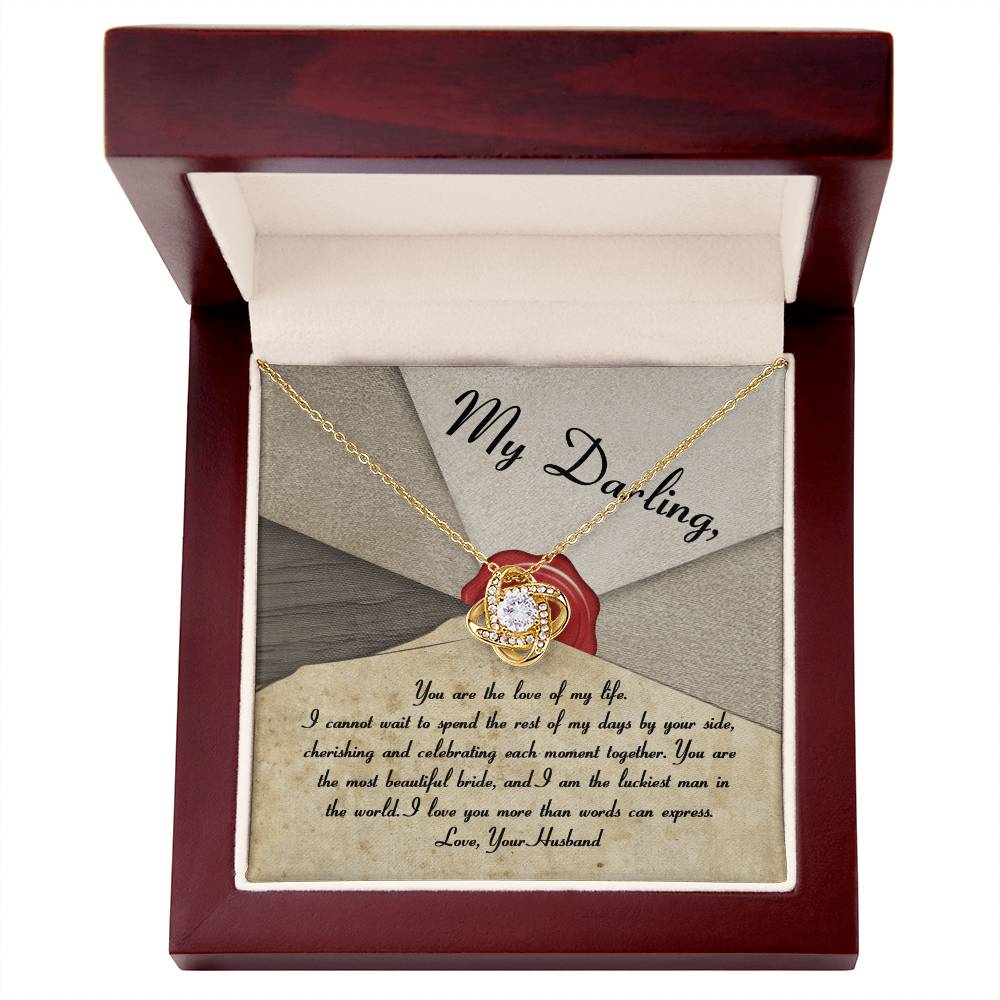 A silver To Bride, Each Moment Together - Love Knot Necklace adorned with cubic zirconia crystals is displayed on a velvet holder, complemented by an overlay message to a bride from her husband, expressing love and commitment.