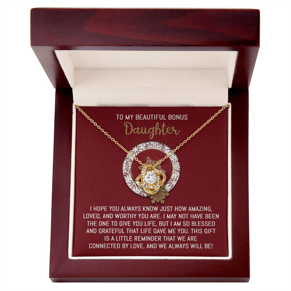 This specially crafted gift, the Bonus Daughter-Always Will Be - Love Knot Necklace, showcases a stunning necklace adorned with cubic zirconia crystals. It comes beautifully packaged in a wooden box featuring floral and decorative designs and includes a touching message for your daughter, making it an ideal way to express your love.