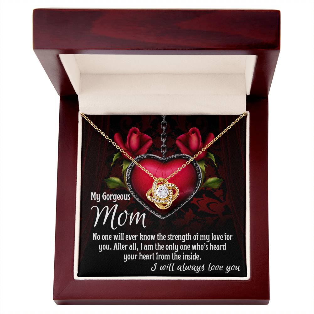 The "[Almost Sold Out] To Mom, Heard Your Heart - Love Knot Necklace" features a heart-shaped pendant adorned with cubic zirconia crystals. It comes nestled in a wooden box with a heartfelt message for "My Gorgeous Mom" expressing love and gratitude, beautifully displayed alongside roses and the elegant Love Knot Necklace design in the background.