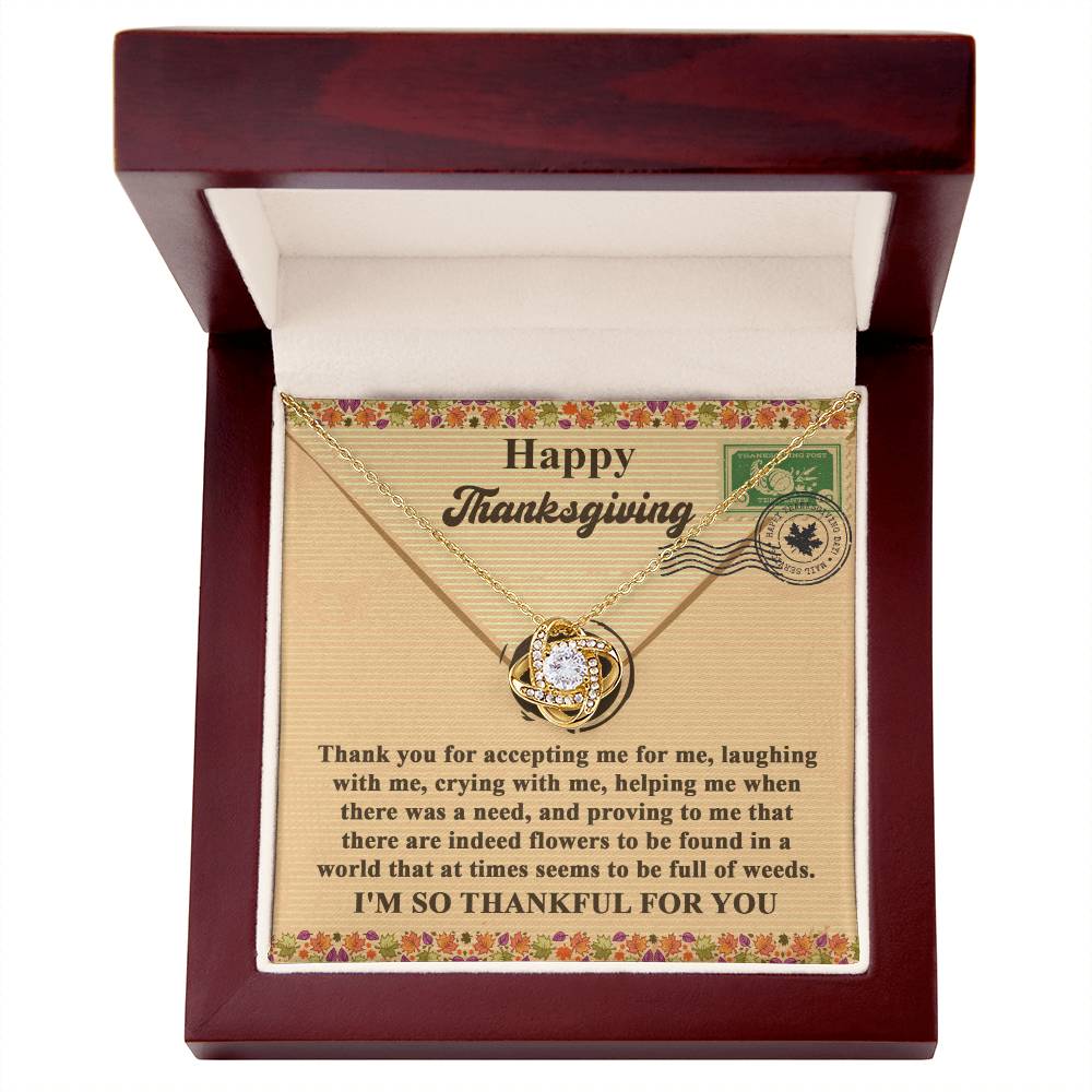 The Thanksgiving-Proving To Me - Love Knot Necklace features a circular pendant elegantly presented in an open box with a wood finish, accompanied by a Thanksgiving card expressing gratitude. The necklace is available in either a white or yellow gold finish and is adorned with sparkling cubic zirconia accents.