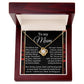 The Mom-By My Side Love Knot Necklace, featuring a circular pendant with a central gemstone and cubic zirconia accents, is elegantly presented in a red jewelry box. The lid bears a heartfelt "Mum" message of gratitude and admiration, making it a personalized gift from the heart.