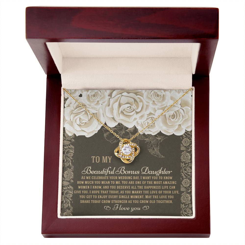 The "To Bonus Daughter, Grow Old Together - Love Knot Necklace" features a gold finish and sparkling cubic zirconia crystals. It comes packaged in a gift box decorated with an ornate floral design and includes a heartfelt message for your daughter on her wedding day.