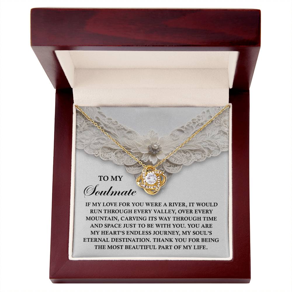 The Soulmate-Eternal Destination - Love Knot Necklace, featuring a central stone and cubic zirconia accents, is nestled in an open red gift box with a heartfelt message on a lace-adorned card and a small flower for that personal touch.