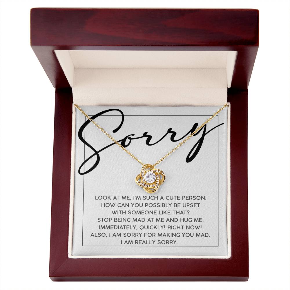 The "Sorry-Someone Like That - Love Knot Necklace" with a white gold finish is displayed in a wooden box. The inside lid of the box features an apology message starting with "Sorry" in large script.