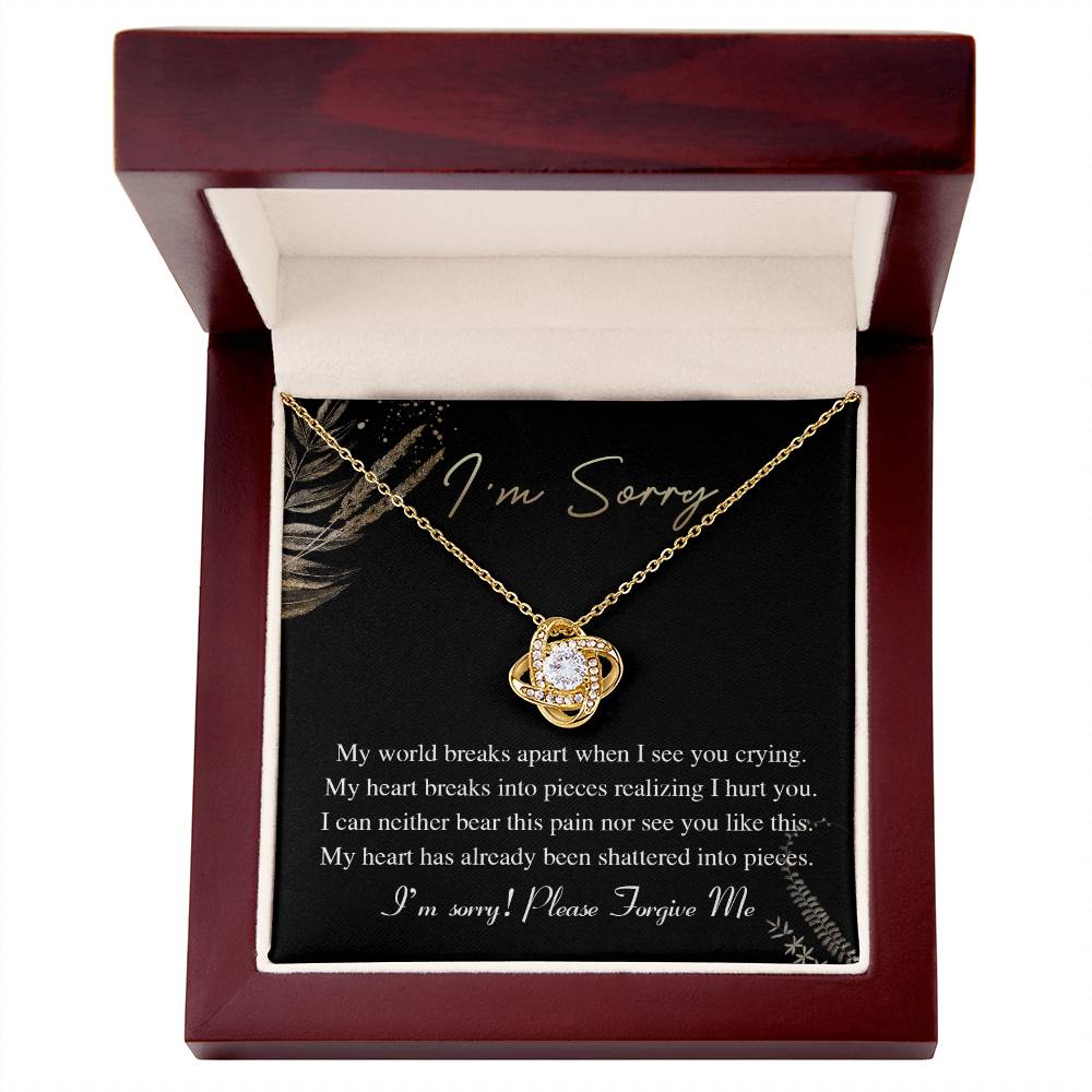 The Sorry-See You Crying - Love Knot Necklace, featuring an intertwined pendant adorned with cubic zirconia crystals, is elegantly displayed on a black card with the inscription "I'm Sorry" and an apology message in white text.