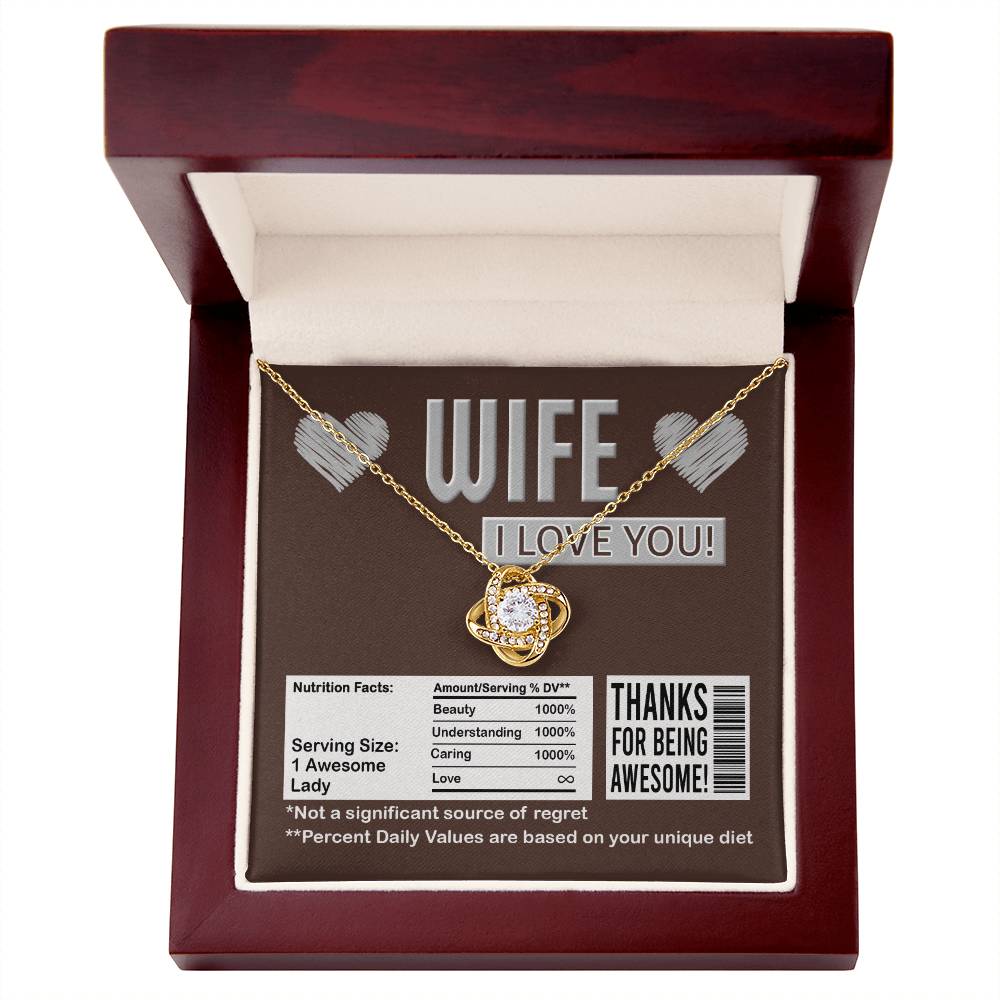 A To Wife, Nutrition Facts - Love Knot Necklace in a gift box that reads, "WIFE I LOVE YOU!" and "Thanks for being awesome!" It humorously lists nutritional facts like "Beauty 1000%" and "Not a significant source of regret," featuring sparkling cubic zirconia crystals with a stunning gold finish.